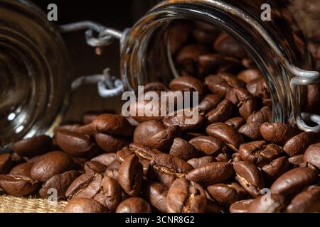 Eine Nahaufnahme, Frontansicht von Kaffeebohnen, die aus einem Glasgefäß kaskadieren. Die satten Brauntöne und die Textur der Bohnen schaffen ein einladendes Bild, perfekt Stockfoto