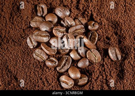 Dieses Bild zeigt einen atemberaubenden Blick von oben auf verstreute Kaffeebohnen, die auf einem reichhaltigen Hintergrund aus fein gemahlenem Kaffee ruhen. Ideal für Kaffeeliebhaber und c Stockfoto