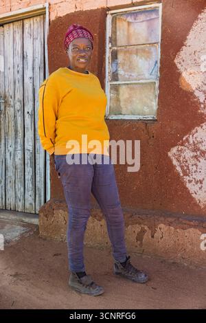 afrika-Dorf, afrikanerin in der Township mit Kopftuch, kalter Tag, draußen auf dem Hof in der Nähe des Hauses, Stockfoto