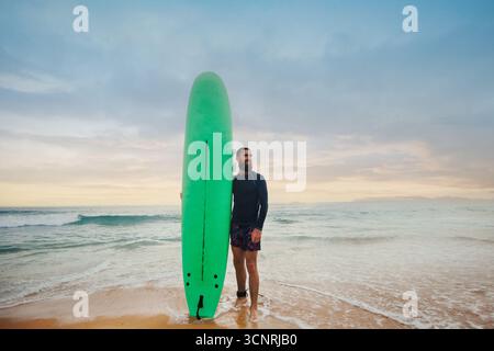 Bärtiger Mann mit Surfbrett in der Nähe eines Strandes. Mann mit Surfbrett im Freien an einem Sommertag Stockfoto