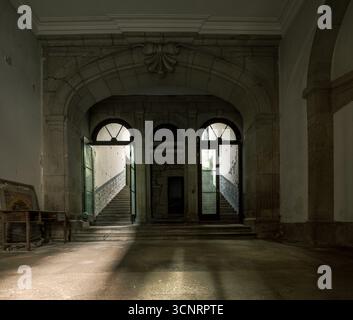 Verlassene historische Treppe mit Steinbögen und dramatischen Lichtbalken im Inneren des alten Gebäudes, geheimnisvolle Lost Place Atmosphäre Stockfoto