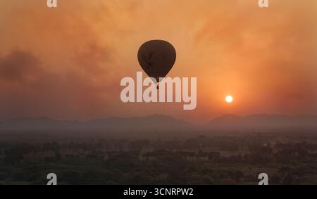 Heißluftballon bei Sonnenaufgang über Bagan mit nebeliger Landschaft mit Bergen und goldenem Himmel in Myanmar, ruhige Reise- und Abenteuerszene Stockfoto