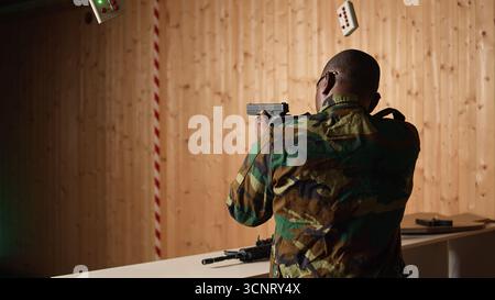 Soldat im Schießstand lädt die Pistole nach, schießt das Ziel und feiert, nachdem er die perfekte Genauigkeit erreicht hat. Militäreinheit im Schießstand übt mit Waffe, jubelt, nachdem er Bullseye getroffen hat, Kamera A Stockfoto