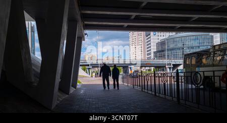 Kiew, Ukraine 10. Mai 2025, Stadtansicht in Kiew mit Silhouetten von zwei Personen, die unter einer Überführung zu Hochhäusern und Verkehr gehen, was das tägliche urbane Leben in der Ukraine widerspiegelt Stockfoto
