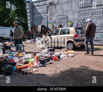 Kiew, Ukraine 11. Mai 2025, Straßenflohmarkt mit Gebrauchtwaren und Vintage-Artikeln auf dem Boden in der Nähe von Auto und Graffiti-Wand, Leute, die alte Kleidung, Werkzeuge und Sammlerstücke durchsuchen Stockfoto