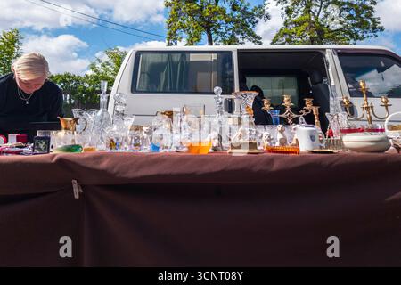 Kiew, Ukraine 11. Mai 2025, lebhafte Flohmarktszene mit Vintage-Glaswaren, Kristallleuchtern und antiken Gegenständen, die an einem sonnigen Nachmittag auf einem Tisch vor einem weißen Van ausgestellt werden Stockfoto