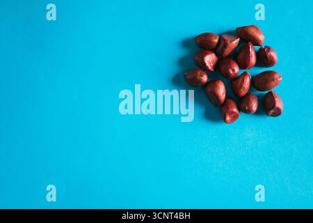 Erdnüsse mit roter Schale, verstreut auf einer blauen Oberfläche und einem Holzlöffel Stockfoto