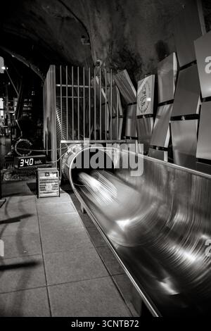 Kinder genießen eine aufregende Fahrt auf der Metallrutsche im Schlossbergtunnel, Teil einer beliebten unterirdischen Attraktion in Graz. Stockfoto