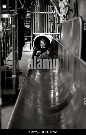 Kinder genießen eine aufregende Fahrt auf der Metallrutsche im Schlossbergtunnel, Teil einer beliebten unterirdischen Attraktion in Graz. Stockfoto
