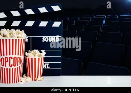 Eimer mit frischem Popcorn und Filmklatscher auf dem Tisch im dunklen Kino Stockfoto