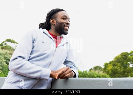 Afroamerikaner lehnt sich an Betongeländer und blickt direkt auf die Gartenterrasse Stockfoto