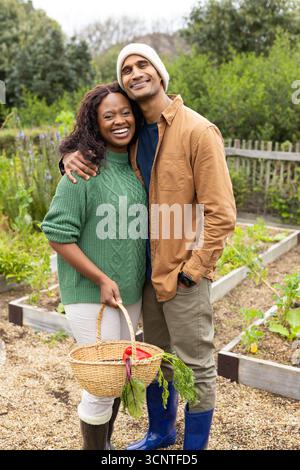 Verschiedene Paare stehen zwischen Hochbeeten und halten Korb gefüllt mit Rüben im eigenen Garten Stockfoto