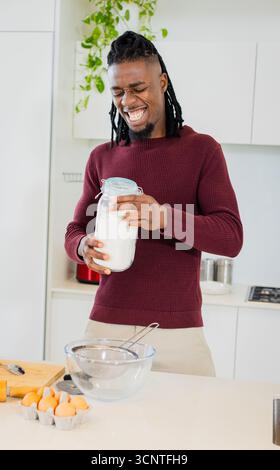 Afroamerikaner grinst, während er ein großes Glas Mehl an der modernen Küchentheke öffnet Stockfoto
