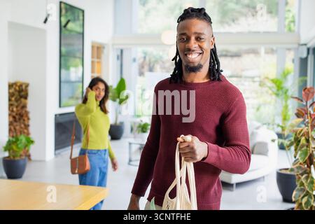 Diverse Paare, die am Telefon sprechen und Canvas Tragetasche im Wohnzimmer mit Brennholz tragen Stockfoto
