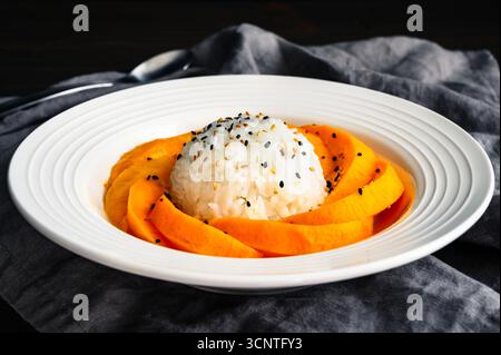 Mango Sticky Reis mit Kokosnusssauce in einer flachen Schüssel Seitenansicht: Thailändisches Dessert mit klebrigem Reis, frischem Obst und gerösteten Sesamsamen Stockfoto