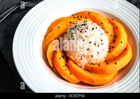 Mango Sticky Reis mit Kokosnusssauce in einer flachen Schüssel Nahaufnahme: Thailändisches Dessert mit klebrigem Reis, frischem Obst und gerösteten Sesamsamen Stockfoto