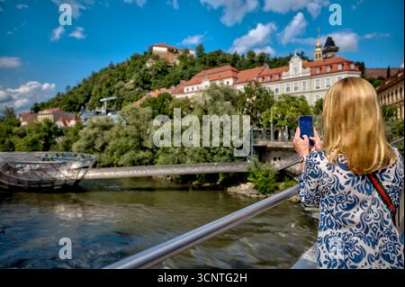 Ein Tourist fotografiert die berühmte Murinsel und den Schlossberg in Graz Stockfoto