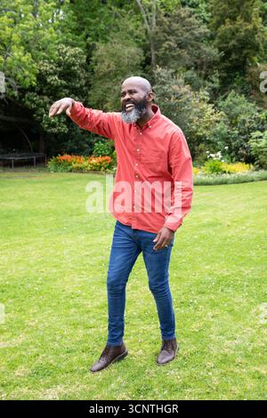 afroamerikaner Senior-Mann in roten Hemd-Jeans lacht und Gesten im Garten nahe dem Trampolin Stockfoto