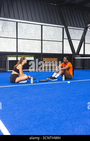 Verschiedene Fitnesspartner in Sportbekleidung auf dem Platz mit Wasserflaschen und Tennisausrüstung Stockfoto