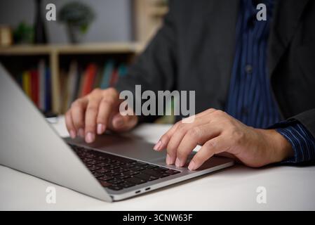 Geschäftsmann mit Laptop im Büro mit Bücherregal Hintergrund. Das Konzept der Wissensarbeit, Produktivität und digitalen Online-Arbeitswirtschaft in Professi Stockfoto