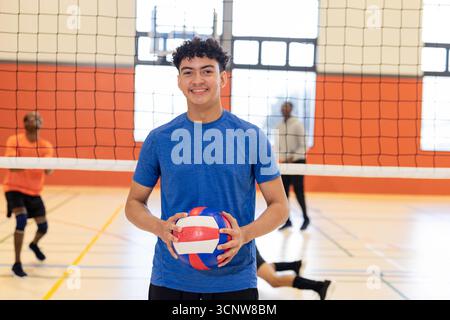 Hispanischer Mann, der Volleyball hält und zielt, dient auf dem Fitnessplatz mit Netz, Feldlinien Stockfoto