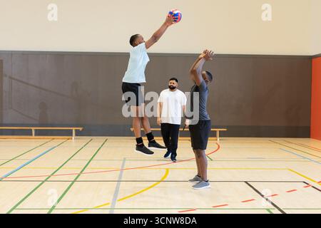Verschiedene männliche Teamkollegen üben Volleyball auf dem Fitnessplatz mit Bank, farbigen Feldlinien Stockfoto