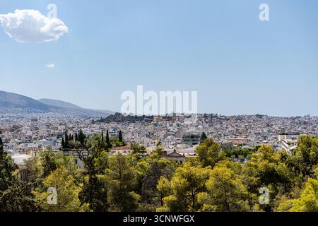 Ein Panoramablick auf die Stadt Athen mit weißen Gebäuden, die über die Landschaft verstreut sind. Im Vordergrund ist üppiges Grün zu sehen, das sich in den Ur verschmilzt Stockfoto