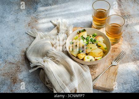 Ein köstlicher griechischer Kartoffelsalat, garniert mit Kapern und geschnittenen Zwiebeln, serviert in einer eleganten Schüssel auf einem Holzbrett mit zwei Gläsern Tee und einem Fass Stockfoto