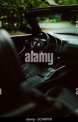 Fahrersitz und Armaturenbrett eines Sportwagens in Schwarz mit schwarzem Lederinnenraum und Metallic-Details, fotografiert in einem bewaldeten Außenbereich Stockfoto