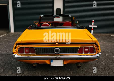 Ein klassisches gelbes Cabriolet parkt elegant vor einer Garage mit weißen Türen. Die lebendige Farbe unterstreicht den Vintage-Stil und die Zeitschriften Stockfoto