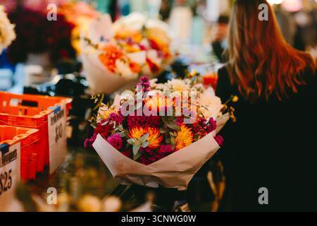 Ein geschäftiger Blumenmarkt in Seattle bietet lebhafte Herbststräuße in einer lebhaften Umgebung. Shopper stöbern durch bunte Blüten und fangen das essen ein Stockfoto