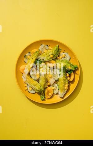 Ein lebhafter Salat auf einer gelben Platte, mit frischem Gemüse, Gurkenscheiben, Pflaumen, Mais, und ein wenig Sesamsamen, die einen anbieten Stockfoto