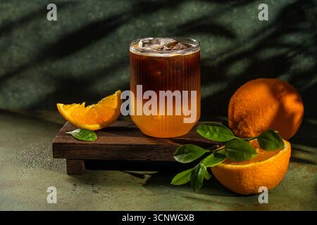 Ein erfrischendes Glas Eiskaffee sitzt elegant auf einem Holzbrett, garniert mit frischen Orangenscheiben. Die lebendigen Farben und Texturen Stockfoto