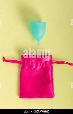 Das Bild zeigt eine blaue Menstruationstasse und einen leuchtend pinkfarbenen Satinbeutel, der nachhaltige Pflegelösungen für die Periode hervorhebt. Perfekt für umweltbewusste Verbraucher Stockfoto