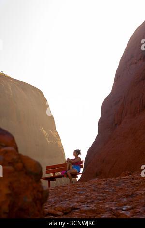 Eine Frau im ruhigen Sonnenaufgang im Uluru Kata Tjuta National Park in Australien, mit dem goldenen Licht, das die legendären roten Sandsteinformationen, Crea, hervorhebt Stockfoto