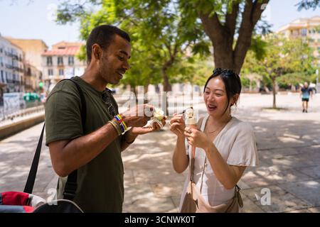 Ein fröhliches Paar genießt an einem sonnigen Tag auf einem belebten Stadtplatz ein Eis, um die Sommerstimmung zu genießen und unvergessliche Erinnerungen in einer Stadt zu schaffen Stockfoto
