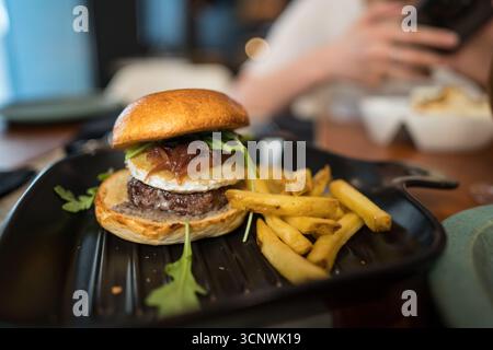 Ein köstlicher Gourmet-Burger mit saftigem Rindfleisch, karamelisierten Zwiebeln und frischem Rucola serviert auf einem gerösteten Brötchen, begleitet von knusprigem goldenem französischem Fisch Stockfoto