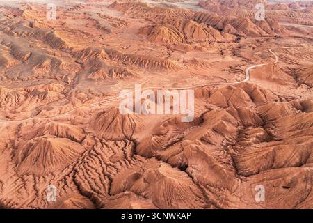Aus der Vogelperspektive einer kurvenreichen Straße, die durch das zerklüftete rötliche Gelände von La Puna, Argentinien, führt und die markanten geologischen Formationen von Th hervorhebt Stockfoto