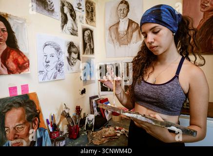 Eine junge Malerin arbeitet leidenschaftlich in ihrem Atelier, umgeben von ihren Kunstwerken und Werkzeugen. Sie mischt sorgfältig Farben auf ihrer Palette und verkörpert sie Stockfoto