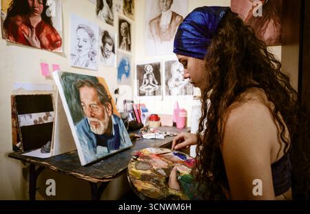 Eine junge Malerin konzentriert sich intensiv auf ihre neueste Kreation in einem lebendigen Atelier, umgeben von Kunstwerken, die ihre Leidenschaft zum Ausdruck bringen Stockfoto