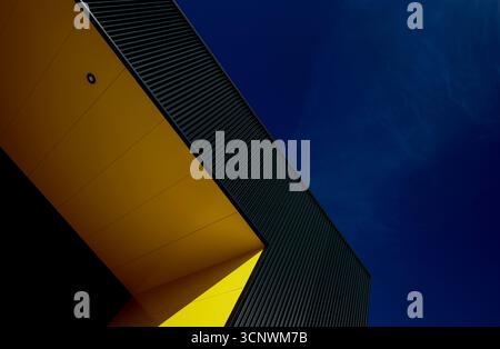 Ein beeindruckendes, modernes Architekturbild zeigt eine auffällige Struktur mit leuchtenden gelben Paneelen, die sich von einem tiefblauen Himmel abheben und ein dramatisches V erzeugen Stockfoto