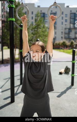 Eine entschlossene Frau nimmt an Fitnessgeräten im Freien Teil und zeigt Kraft und Konzentration. Ihre Aktivkleidung ist bequem und betont ihn Stockfoto