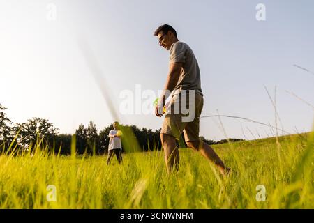Zwei Familienmitglieder teilen einen fröhlichen Moment im Freien. Vater und Sohn spielen spielerische Aktivitäten in einem üppig grünen Feld unter einem klaren blauen Himmel auf einer s Stockfoto