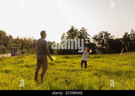 Unter klarem Himmel teilen sich Vater und Sohn einen freudigen Moment beim Fangen auf einem grünen Feld. Die Sonne scheint hell, als sie sich verbinden und Spaß haben Stockfoto
