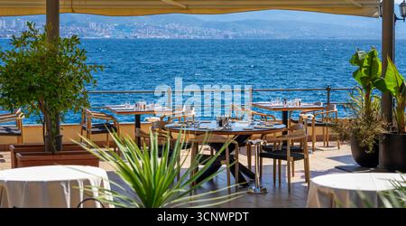 Terrasse des Restaurants am Meer mit Meerblick, Esstisch im Freien und Skyline der Stadt in Opatija Kroatien. Stockfoto
