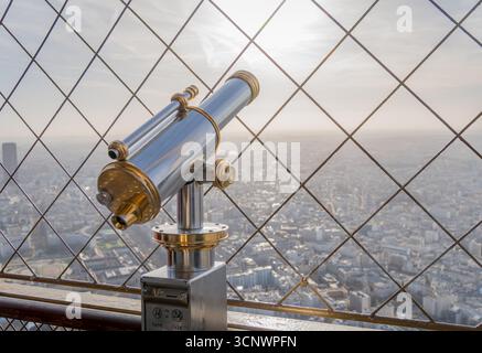 Ein Teleskop überblickt eine atemberaubende Morgenstadt vom Eiffelturm. Die Sonne geht im Hintergrund auf und strahlt ein warmes Licht über Paris Stockfoto