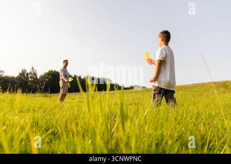 Vater und Sohn verbringen schöne Zeit im Freien auf einem grasbewachsenen Feld. Sie lächeln und spielen mit Seifenblättchen und genießen die Wärme der Sonne auf einem Be Stockfoto
