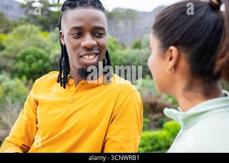 Afroamerikaner und Indianer, die Jacken tragen, sitzen auf der Bank im Park und unterhalten sich über den Tag Stockfoto