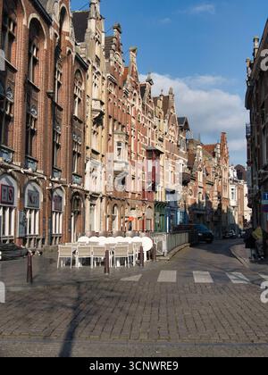 Kopfsteinpflasterstraße mit historischen Gebäuden in Gent - Blick auf eine malerische Kopfsteinpflasterstraße mit historischen Backsteinfassaden und einer Caféterrasse Stockfoto