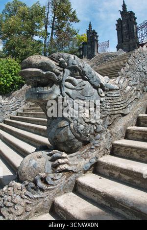Verzierte Steindrachenstatue, die die Tempeltreppe bewacht - Eine detaillierte Nahaufnahme eines verwitterten Steindrachen auf einem Treppengeländer, das zu einem Pago führt Stockfoto